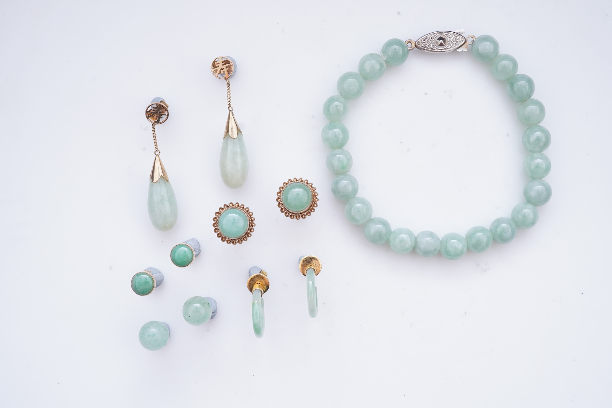 A collection of jadeite jewels, comprising: a bead bracelet with a silver clasp; together with three pairs of studs; one pair of hoop studs, one broken and restuck; and one pair of drop earrings, each set with jadeite, m